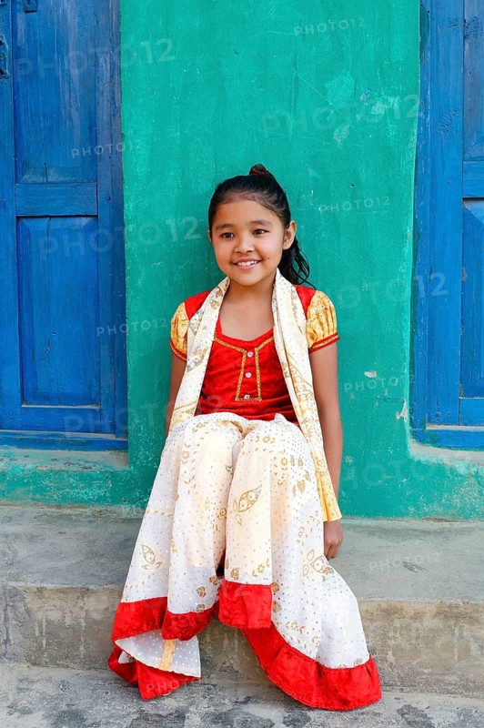 Smiling Nepalese girl seated on steps in front of a colorful house