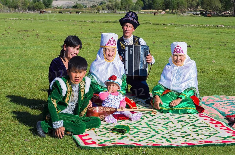 Kazakh family in traditional clothes listening to the music of an accordion player