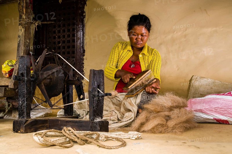Native woman spinning sheep's wool with traditional spinning wheel in front of house