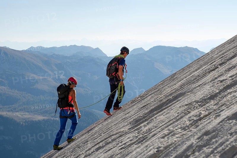Mountain guide guiding a young woman on a short rope through a rock face