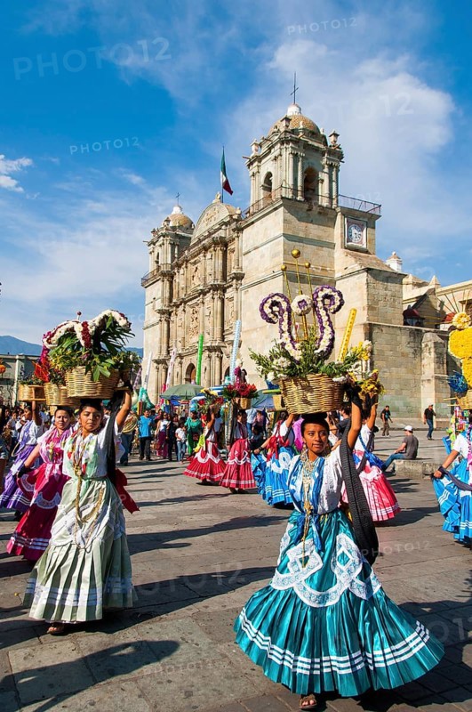 Women in traditional dresses with flower baskets dancing on the main square Zocalo in front of church Santo Domingo de Guzman