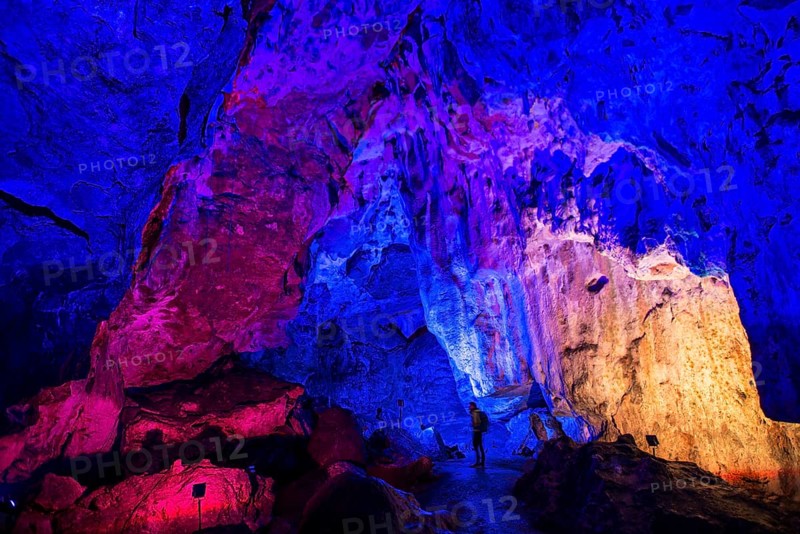 Young man looks at colorfully illuminated stalactite cave