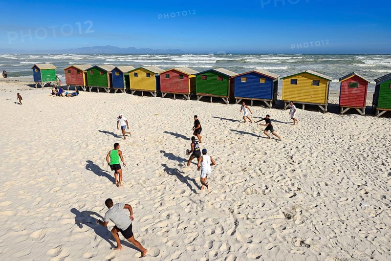 Teenagers play rugby in front of colourful beach houses