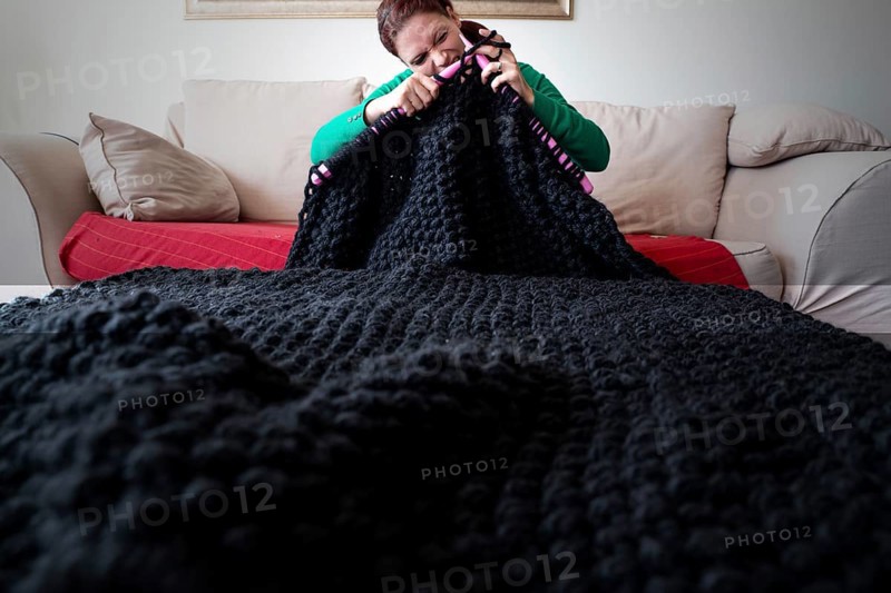 Woman knitting a blanket with large knitting needles
