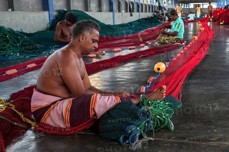 Local men repairing fishing nets in hall at harbour