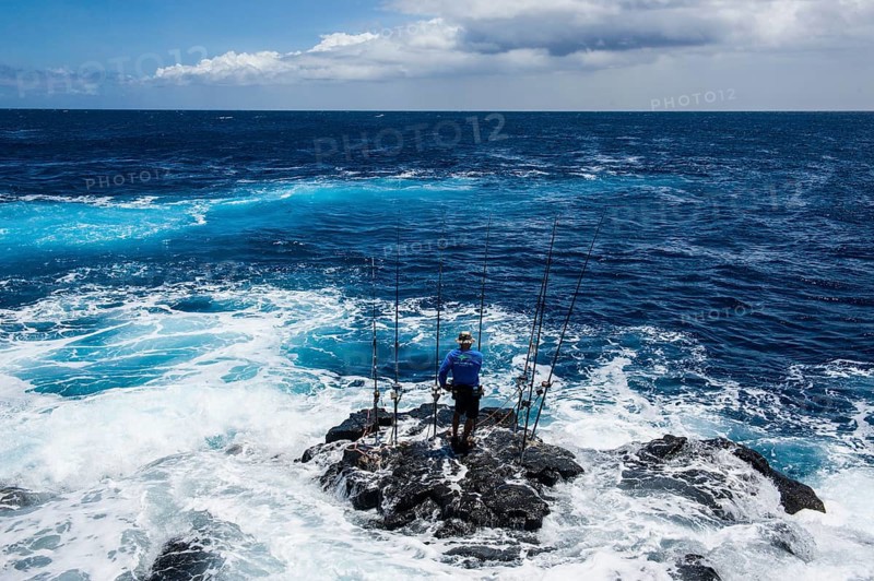 Fisherman standing on a rock in The Sea with his angling rods