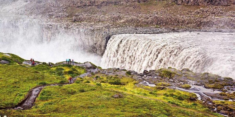 Hikers at the edge of the Dettifoss waterfall with falling water masses