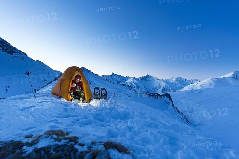 Snowshoe hiker in tent eating in the snow on the Madelejoch
