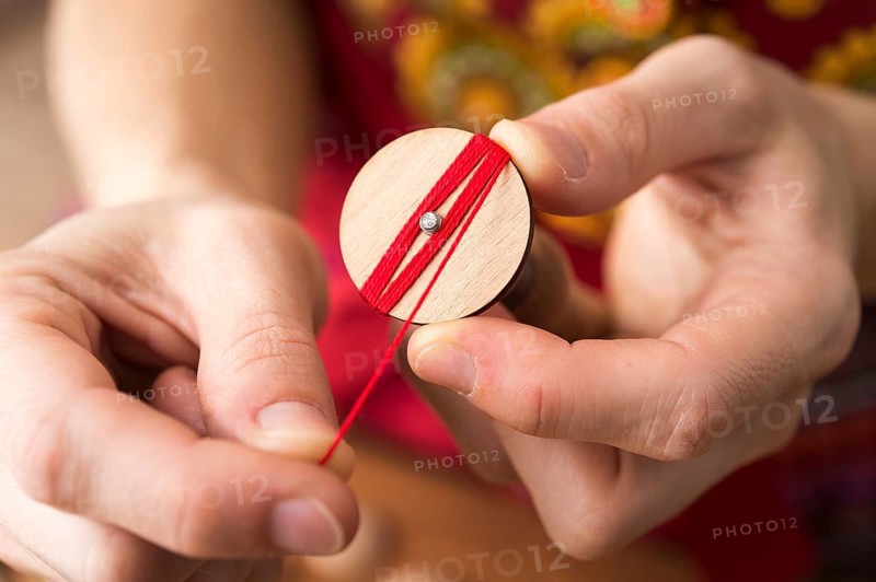 Button maker in the second step of Posamentenknopfe production holding wooden blank and carefully wrapping red yarn