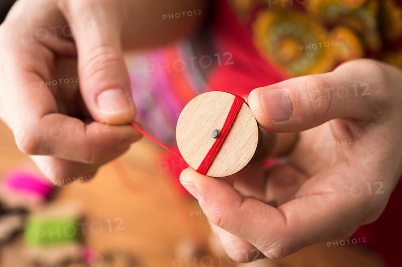 Button maker holding wooden blank and wrapping red yarn