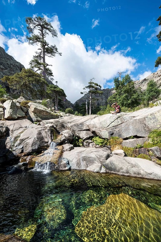 Young man sitting next to a pool with small waterfall in the mountains