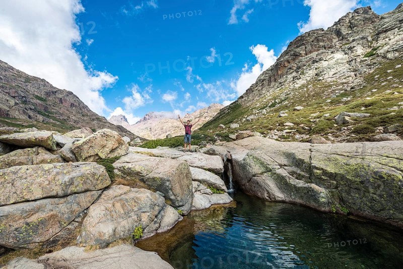 Young man standing next to a small waterfall with pool in the mountains