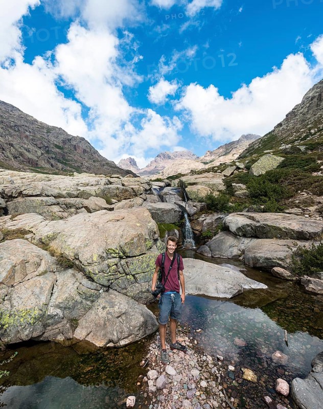 Young man standing at a pool with a small waterfall in the mountains