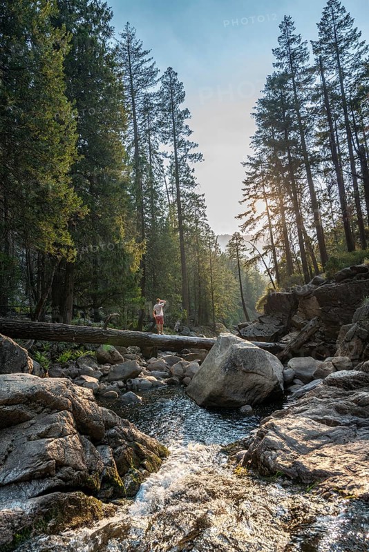 Young man crossing a tree trunk over the Merced River