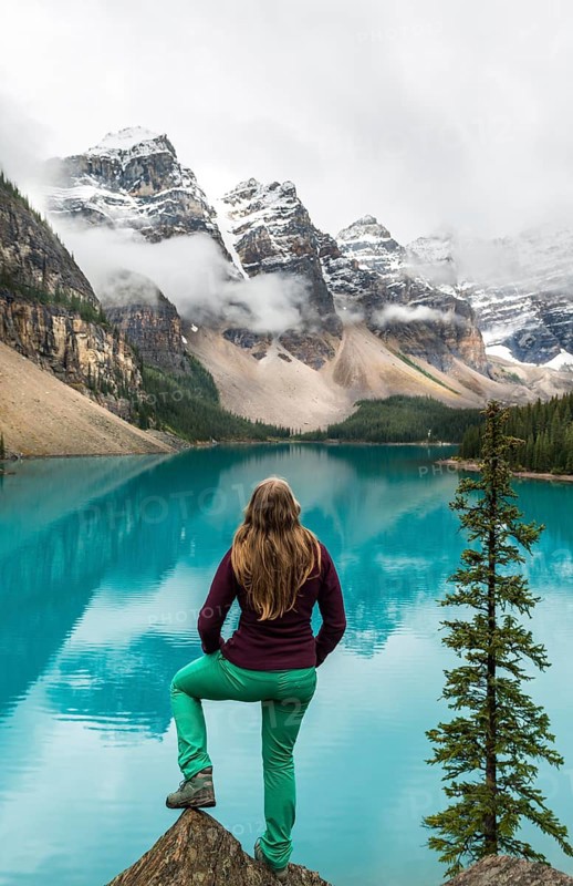 Young woman standing in front of a lake looking into mountain scenery