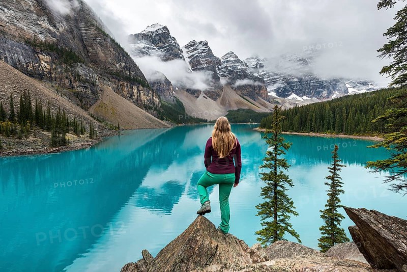 Young woman standing in front of a lake looking into mountain scenery