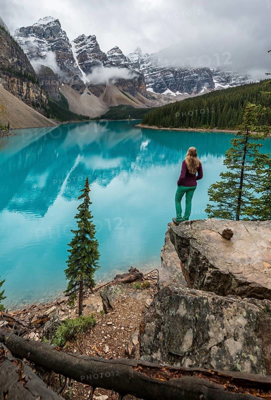Young woman standing in front of a lake looking into mountain scenery