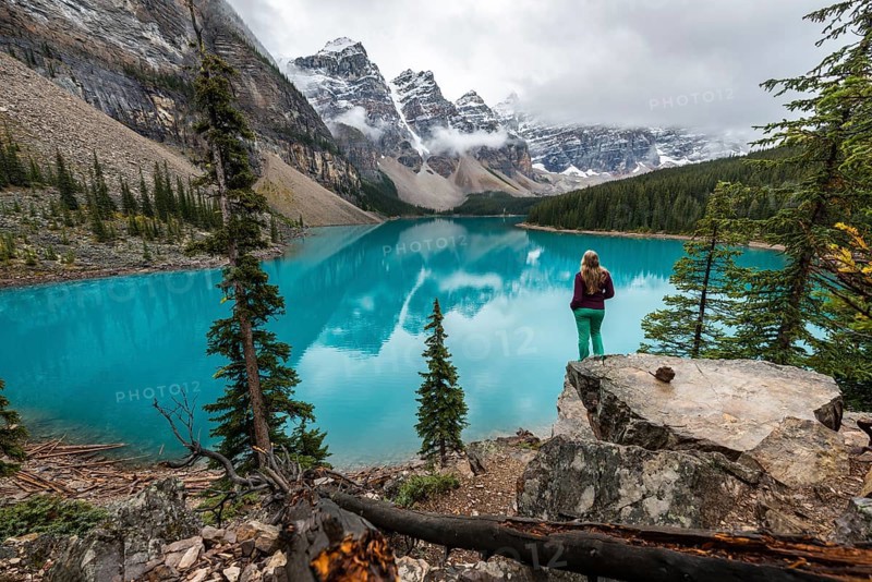 Young woman standing in front of a lake looking into mountain scenery