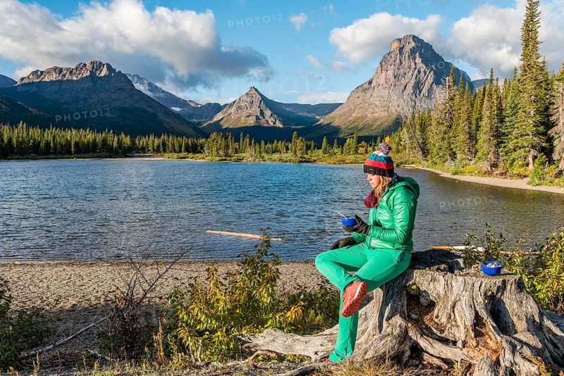 Young woman with breakfast at the mountain lake Two Medicine Lake in mountain landscape