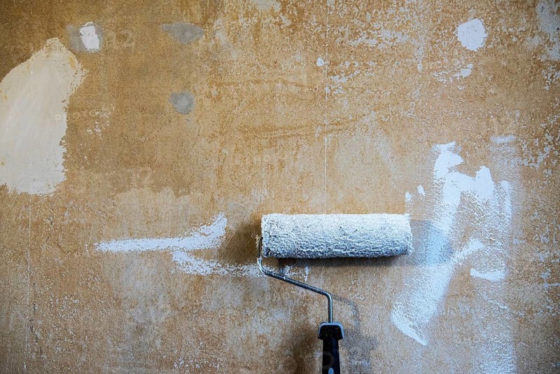 Painter's roller with white paint leaning against a plastered wall