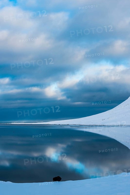 Snow-covered coastal landscape with water reflection