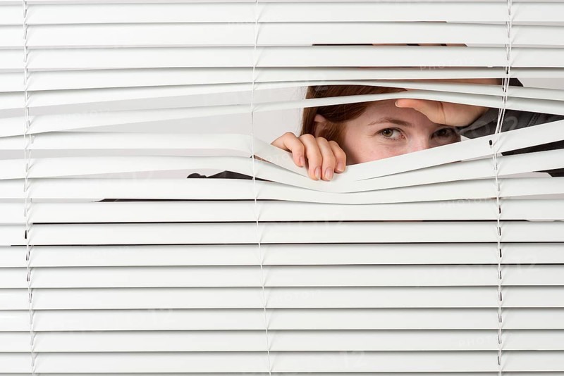 Young woman looking through blinds