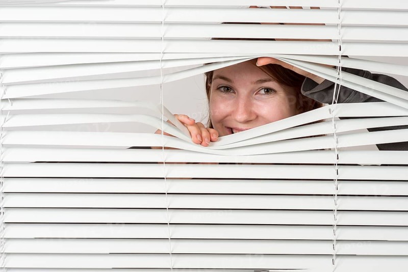 Young woman looking laughing through blinds