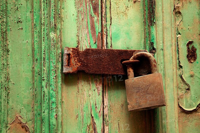 Rusty door lock with deadbolt on weathered wooden door with green paint