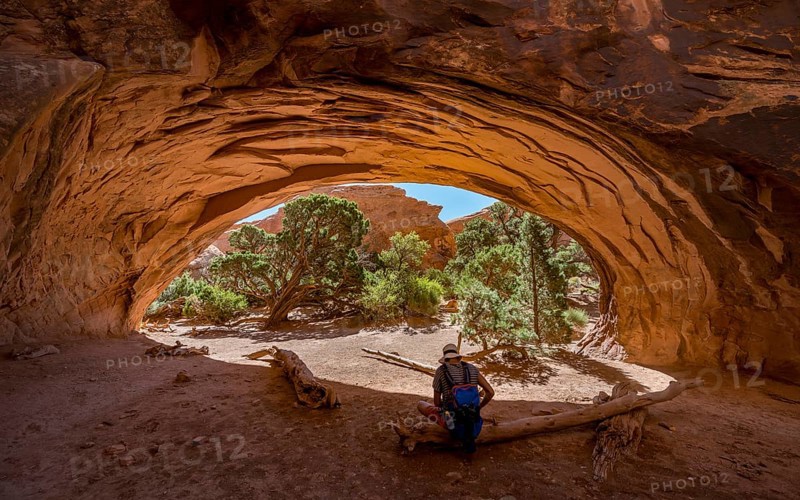Young man sitting under rock arch