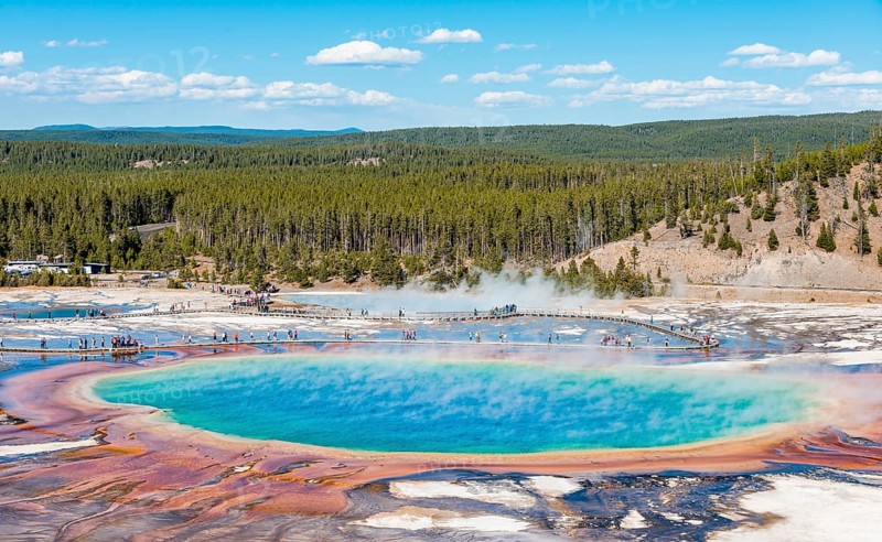 Visitors on footbridge over steaming hot spring with coloured mineral deposits