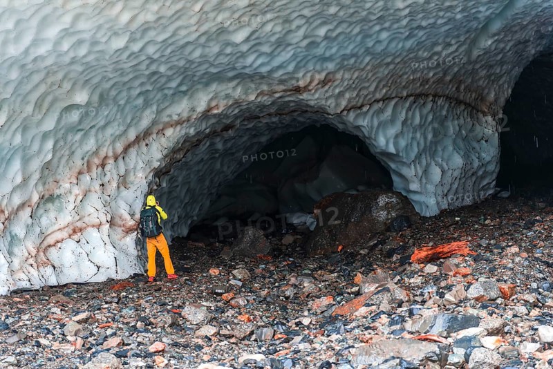 Man at the entrance of an ice cave of a glacier