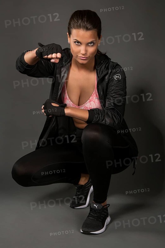 Young woman with dark hair tied together poses in a sporty outfit