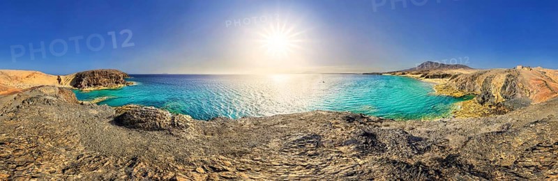 Panorama with sun on rocky coast with turquoise waters of Playa del Papagayo