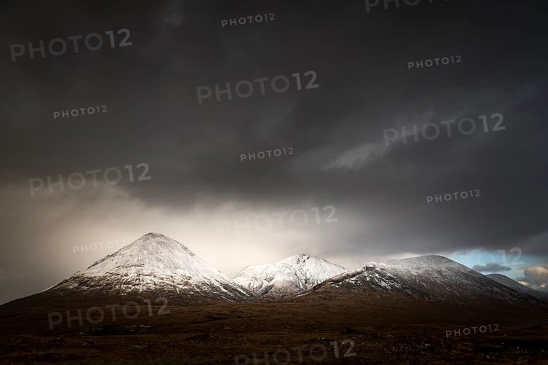 Moor landscape with snow-covered peaks of the Cullins Mountains in front of dramatic clouds in Highland Landscape