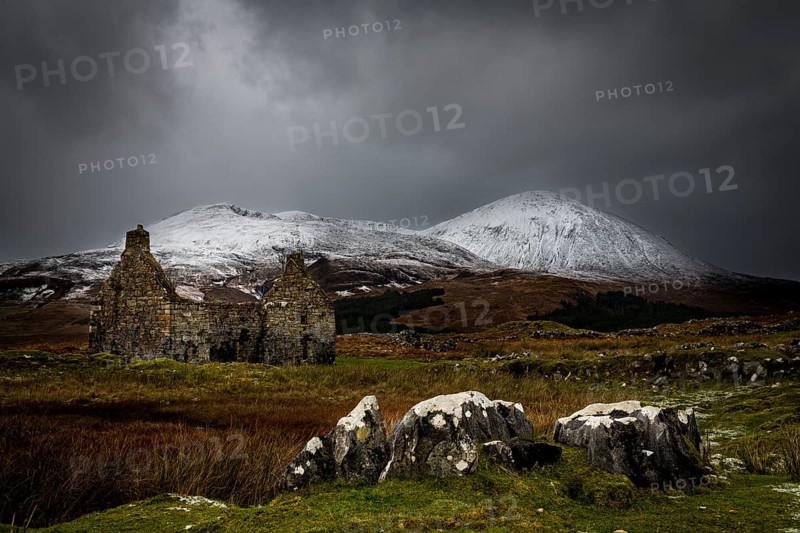Rocks with white caps and house ruin in Highland landscape with snowy Cullin mountains in the background