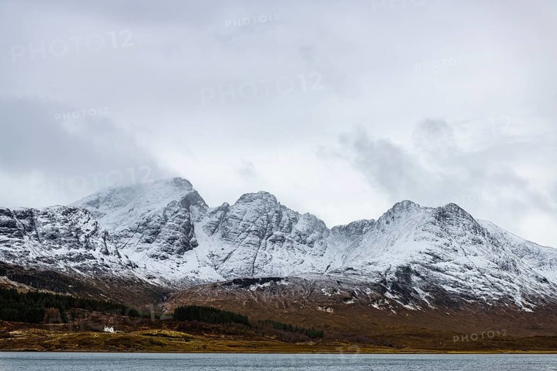 Loch Slapin with small house in Highland landscape with snowy Cullin mountains in the background
