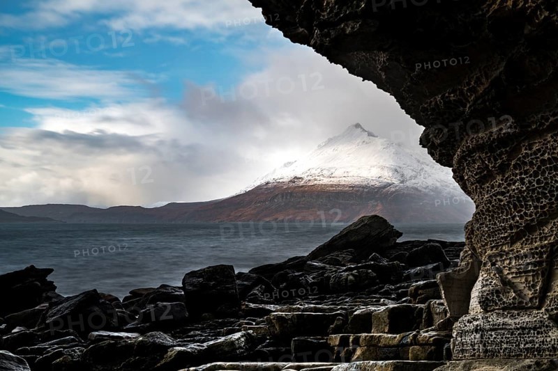 Big rocks in the water of the North Sea with snow-covered Cullin mountains in the background