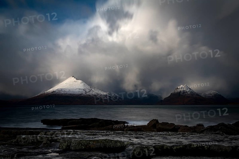 Big rocks in the water of the North Sea with snow-covered Cullin mountains in the background