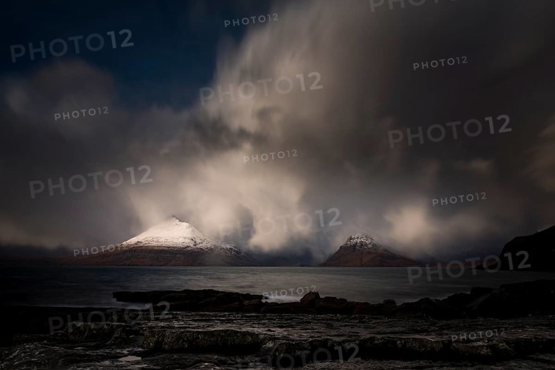 Big rocks in the water of the North Sea with snow-covered Cullin mountains in the background