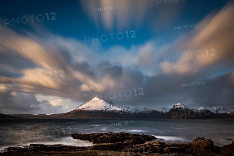 Big rocks in the water of the North Sea with snow-covered Cullin mountains in the background