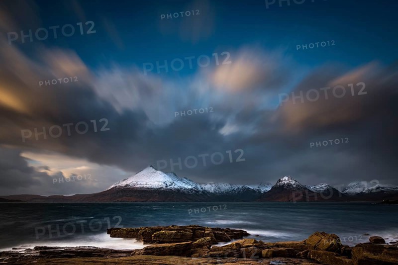 Big rocks in the water of the North Sea with snow-covered Cullin mountains in the background