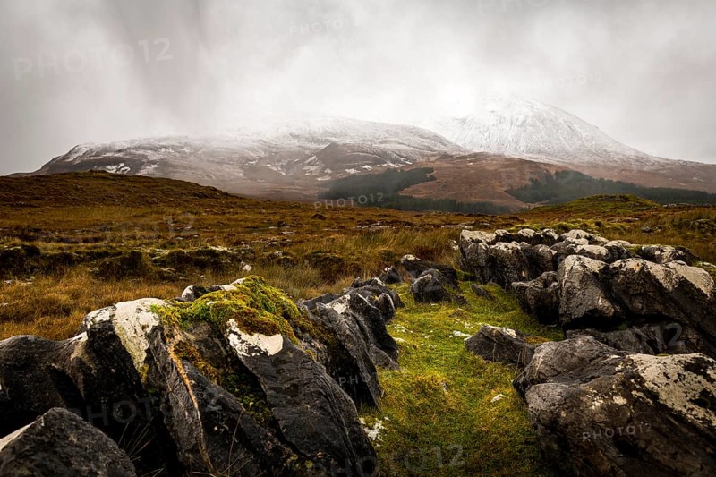 Dark rocks with white caps in Highland landscape with snow-covered Cullin mountains in the background