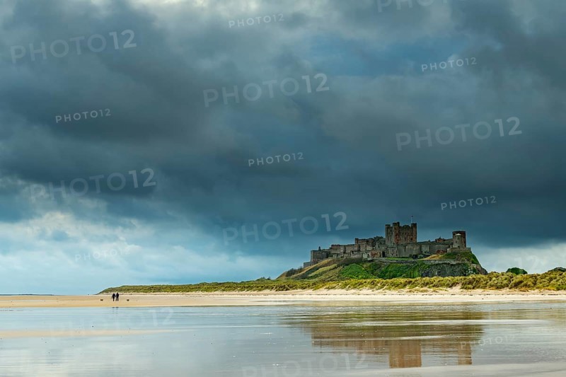 Flat sandy coast with Bamburgh Castle and reflection in the water with dark clouds