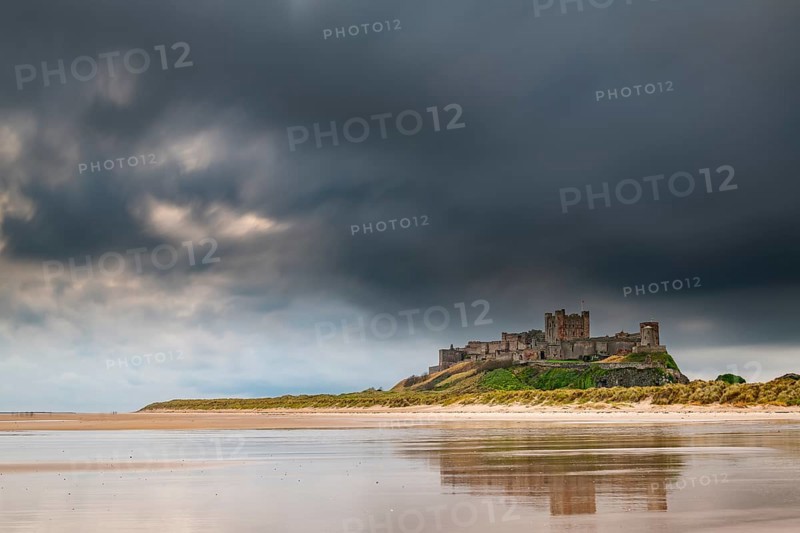 Flat sandy coast with Bamburgh Castle and reflection in the water with dark clouds