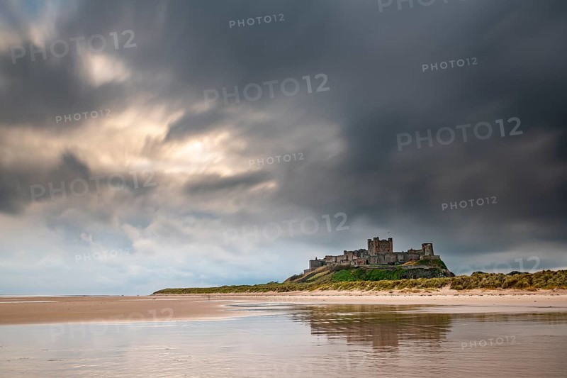 Flat sandy coast with Bamburgh Castle and reflection in the water with dark clouds