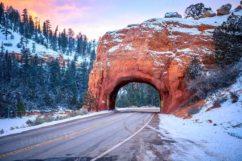 Road with tunnel through red rock arch in snow