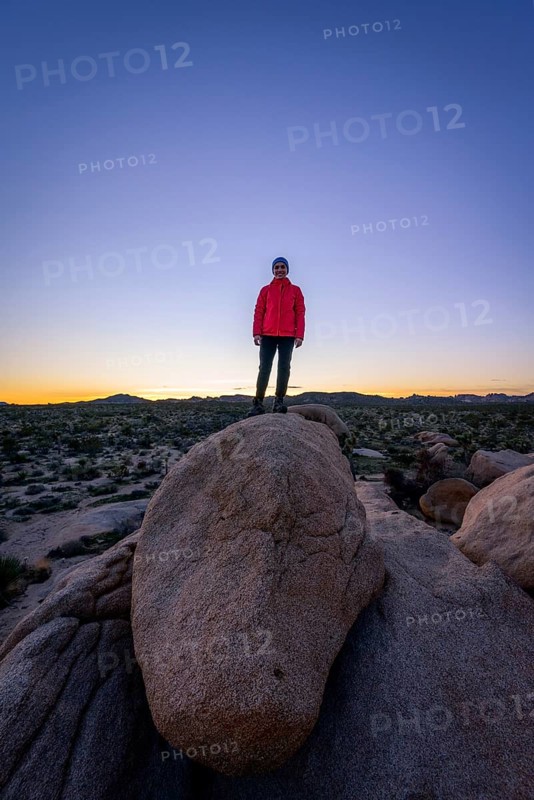 Young woman standing on round granite rocks at sunset