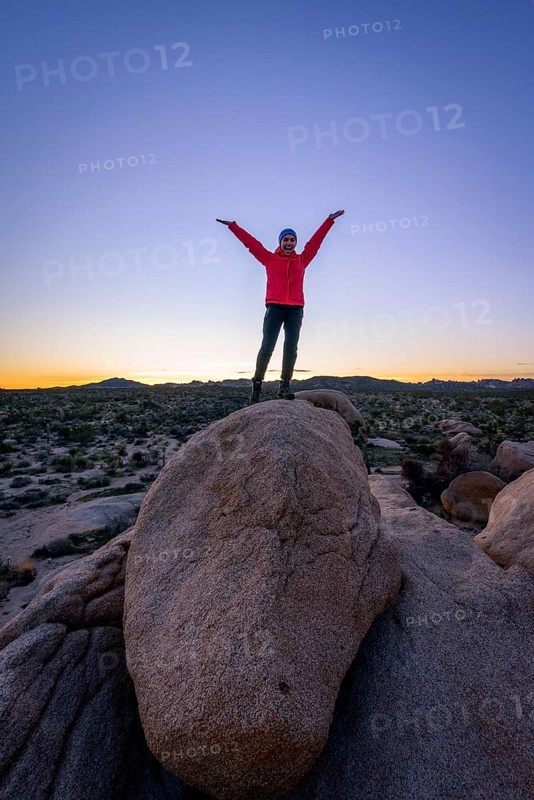 Young woman standing with outstretched arms on round granite rocks at sunset
