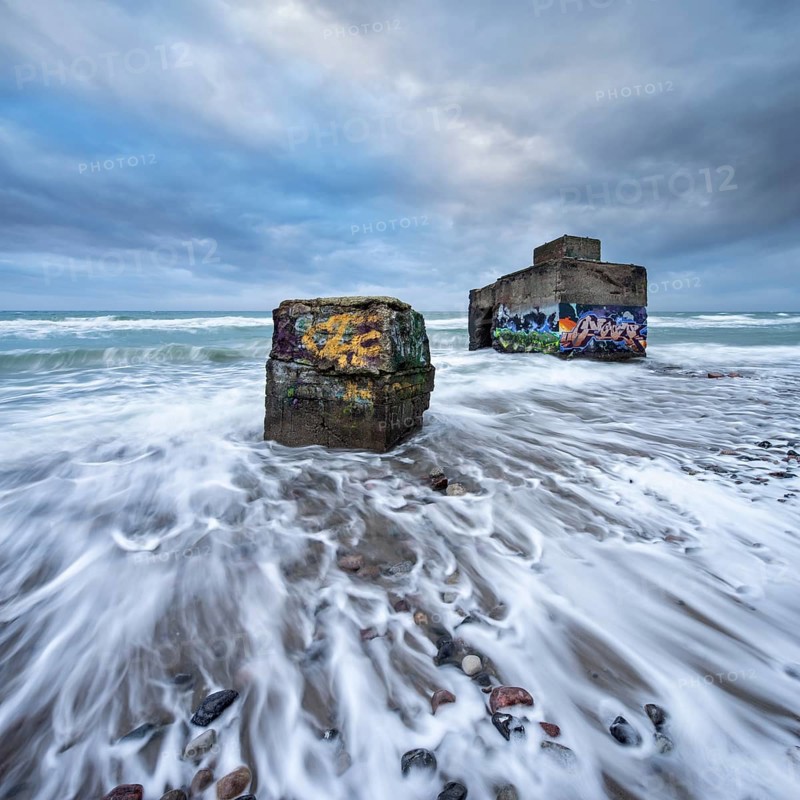 Old bunkers with graffiti in the surf of the Baltic Sea below the steep coast at stormy sea