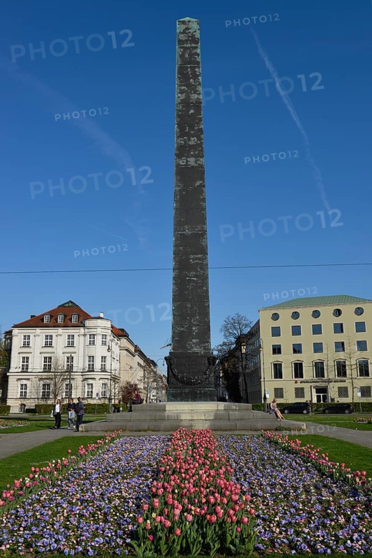Obelisk with flower bed in front of houses roundabout